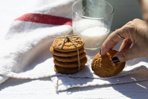 Hand picking a cookie from a stack next to a glass of milk on a white cloth Stock-Fotos