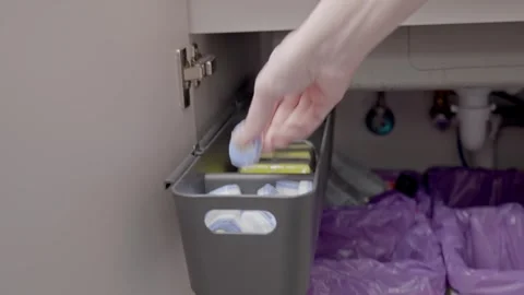 Hand picking dishwasher detergent tablet from container under kitchen sink Stock Footage 328197710