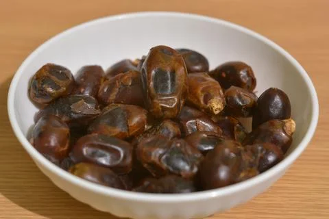 Hand picking dried dates from white bowl on wooden table 库存照片