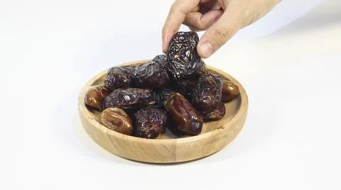 Hand Picking Dried Dates from Wooden Bowl on White Background Stock Photos