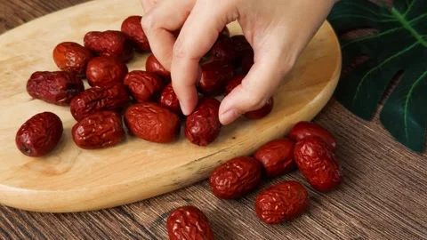 Hand picking up dried red dates from a wooden cutting board on a dark wood Stock Footage 331572759