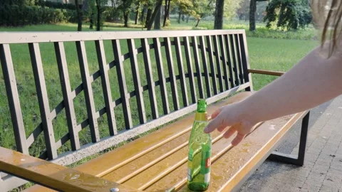 Hand picking up empty glass bottle from a bench in a park cleaning public space  Vídeos de archivo 282514266