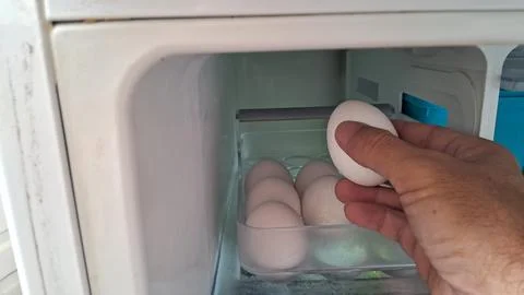 Hand picking a fresh white egg from the refrigerator tray Stock Photos