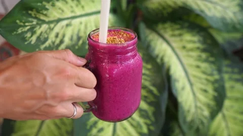 A hand picking a jar of dragon fruit smoothie. Tropical leaves on the background Stock Footage 151950581