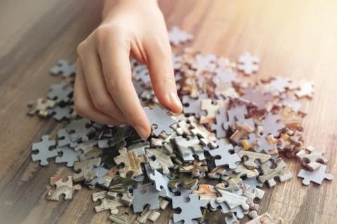 Hand picking one piece of mixed jigsaw puzzle, macro close up Stock Photos