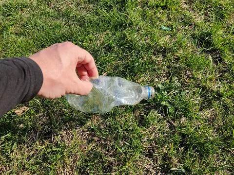 Hand picking up plastic bottle from grass: environmental cleanup action Foto stock