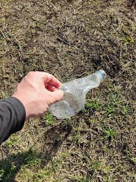 Hand picking up plastic bottle from grass to promote environmental cleanup Foto stock