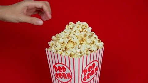 Hand picking popcorn in a classic popcorn box on a red background.Popcorn spinni Stock Footage 196686034