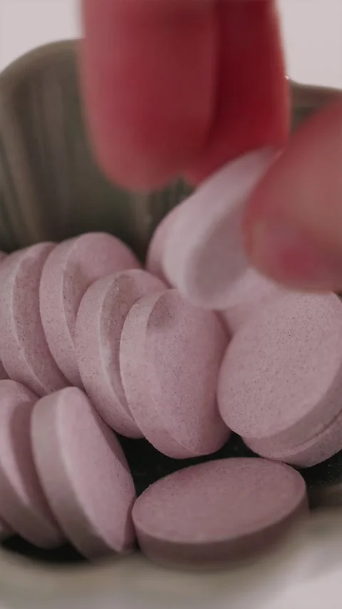 Hand picking up red effervescent tablet from a white bowl Stock Footage 332724594
