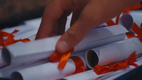 Hand Picking Up Rolled Graduation Diploma Tied with Orange Ribbon Stock Footage 321013918