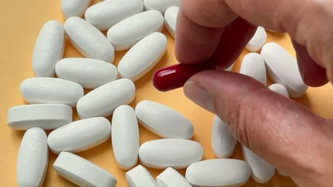 A hand picking up a single red capsule from a pile of white pills Video stock 338186326