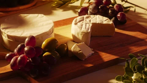 Hand picking up a slice of camembert cheese from a rustic wooden board with Stock Footage 334269795