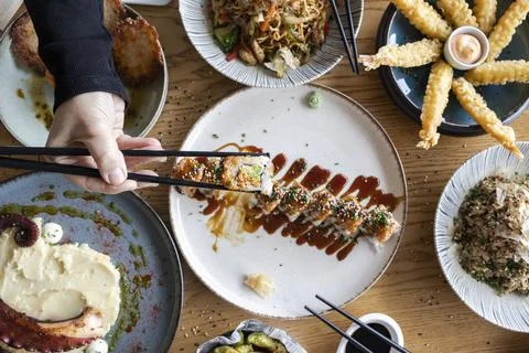 Hand picking sushi roll from table with oriental food Stock Photos