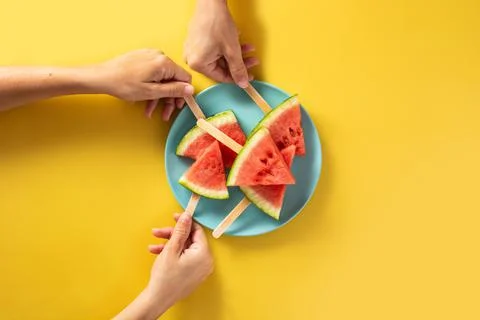 Hand picking up watermelon slices popsicles on blue plate Stock Photos