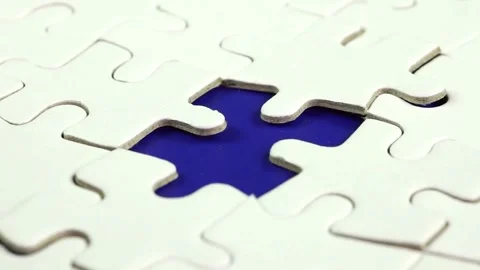 Hand is picking up a white jigsaw puzzle and attaching it to the board Finding a Stock Footage 336248762