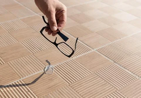 The hand picks up a broken spectacle frame on the street from a tile Foto stock