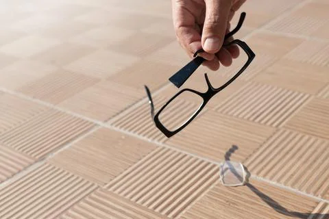 The hand picks up a broken spectacle frame on the street from a tile Foto stock