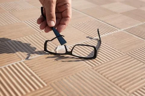 The hand picks up a broken spectacle frame on the street from a tile Stock Photos