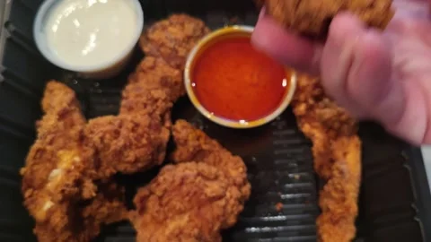 Hand picks crispy fried chicken tenders from black take out tray Stock Footage 340111980