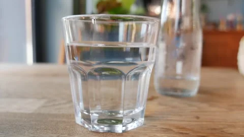Hand picks up glass of water from table, refreshing drink for health. Vídeos de archivo 333029564