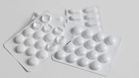 Hand picks up a packet of tablets from a stack of medicine on a white table Stock Footage 119010401
