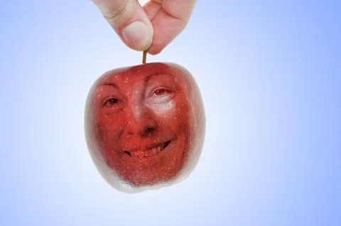 A hand picks a red apple, which also looks just like a cherry with a happy fa Stock Photos