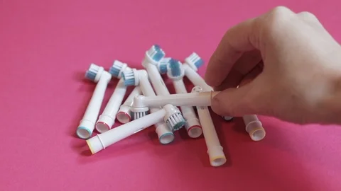 A hand picks up a toothbrush head from a stack on a pink background Stock Footage 117178663