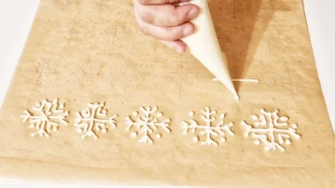 Hand piping white snowflake patterns with icing on parchment paper for baking Stock Footage 327259711