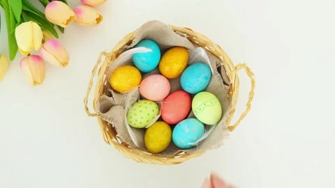 Hand place one egg into a wicker basket with multi-colored Easter eggs Stock Footage 331499526