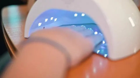 A hand is placed inside a UV nail dryer, showing the drying process of manicure Stock Footage 338447226