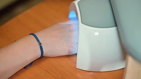 A hand is placed under a UV light device to dry gel nails in a beauty salon. Stock Footage 338447185