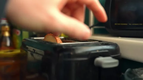 Hand places a bread slice into a toaster in a home kitchen, close-up breakfast Stock Footage 330848086