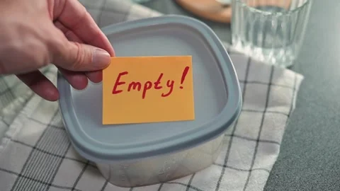 A hand places a bright sticky note labeled Empty on a clear food container in a Stock Footage 339096794