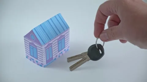 Hand places bunch of keys next to colored paper house on white background. Purch Video stock 247498917