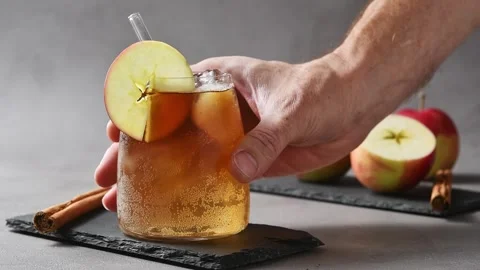 Hand places chilled apple cider cold brew tonic on slate board beside apples and Stock Footage 345556970