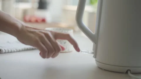 Hand places electric kettle on base and presses power switch on kitchen counter Stock Footage 337434091