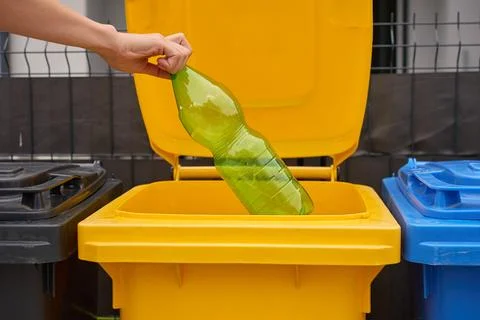 Hand places empty plastic bottle into yellow recycling bin for waste sorting Stock Photos