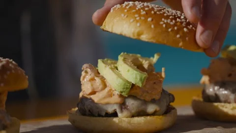 Hand places the final bun over a stack of toppings, completing a burger Stock Footage 247054614