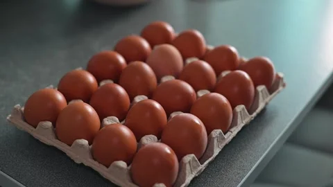 A hand places fresh brown eggs into a carton on a kitchen countertop. Stock Footage 339096229