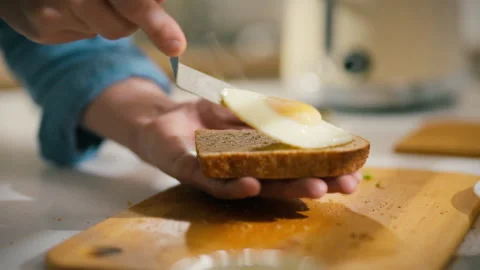 A hand places a fried egg on a slice of whole grain toast. The action takes Stock Footage 304272414
