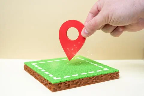 A hand places a geolocation symbol on a plot of land. Selecting a plot for .. Stock Photos
