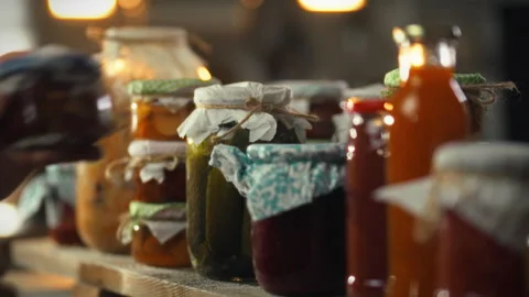 Hand places jar of pickles on a shelf in dimly lit cellar during food preser Stock Footage 331352130