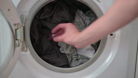 A hand places laundry capsules into the washing machine door. A mix of fabrics 스톡 동영상 337101433