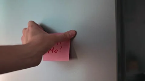 A hand places a pink sticky note with the message Call Me on a smooth surface. Stock-Footage 339096539