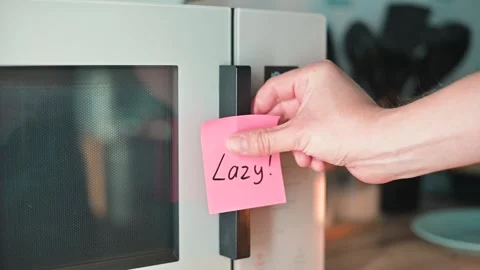 A hand places a pink sticky note LAZY on the door of a microwave. This action Stock Footage 339096681