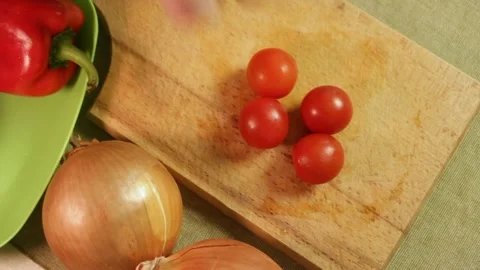 Hand places red cherry tomatoes on wooden board with peppers and onions behind Stock Footage 318602999
