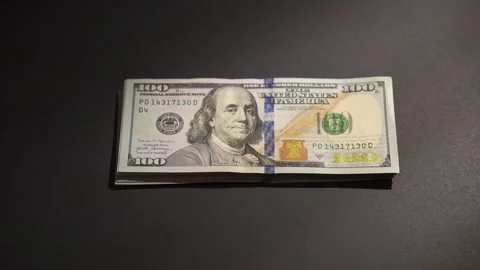 A hand places a stack of 100 dollar bills on a dark surface. Video stock 314382297