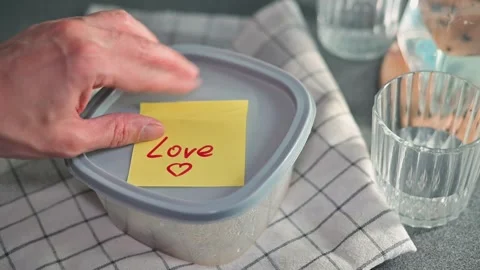 A hand places a sticky note that reads Love on a container filled with food on a Video stock 339096777