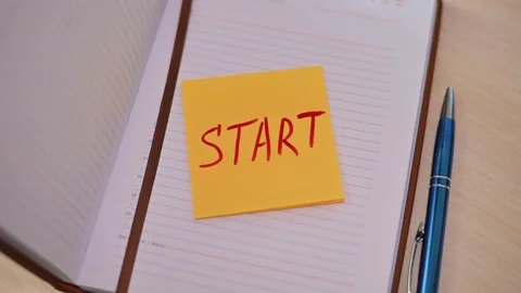 A hand places a sticky note that says start on an empty notebook on a desk. A Stock Footage 339094137
