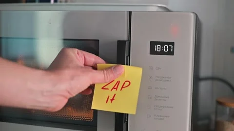 A hand places a sticky note with the word 'ZAP' on a microwave to indicate Stock Footage 339096695